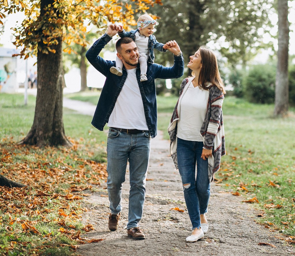 A happy young family walking in a park, baby riding on dad's shoulders