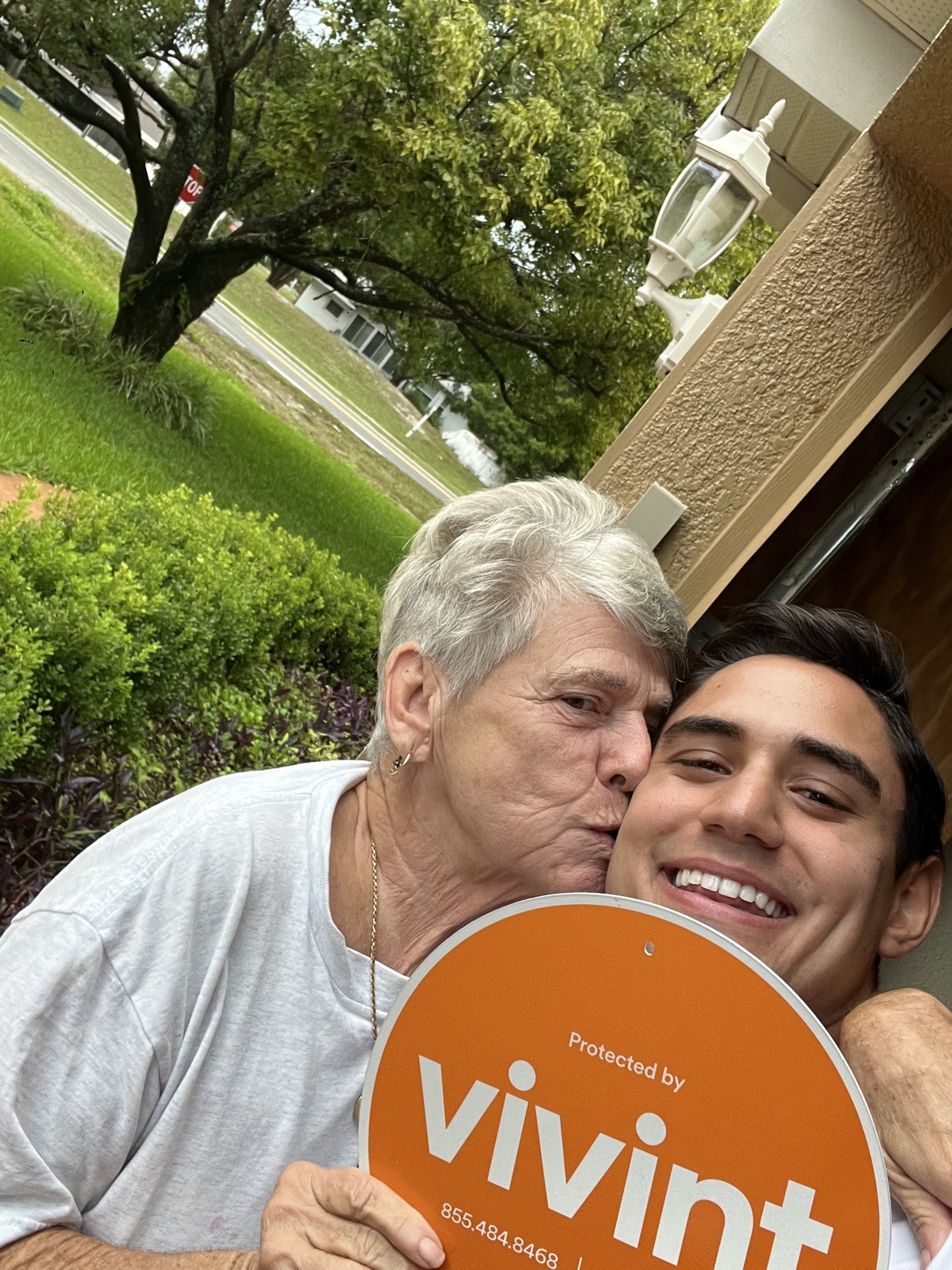 An older customer kissing Matthew on the cheek while holding the orange Vivint sign outside her home