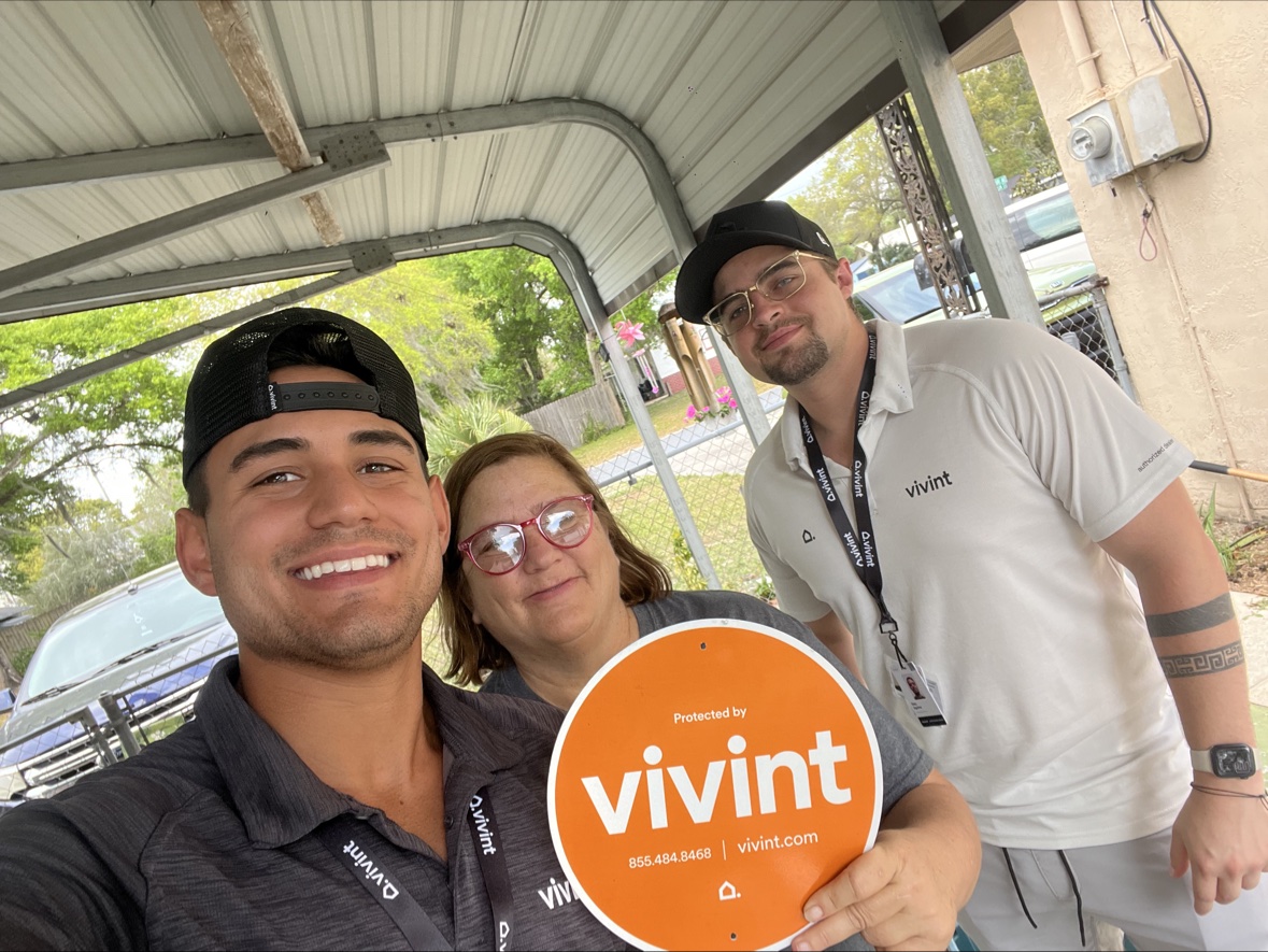 Carport selfie with a customer and a teammate, Vivint sign in hand