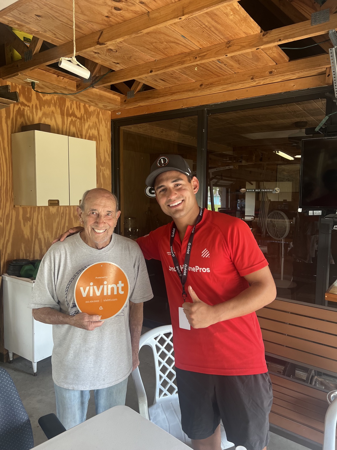 Matthew with an older customer on a porch, both giving a thumbs up