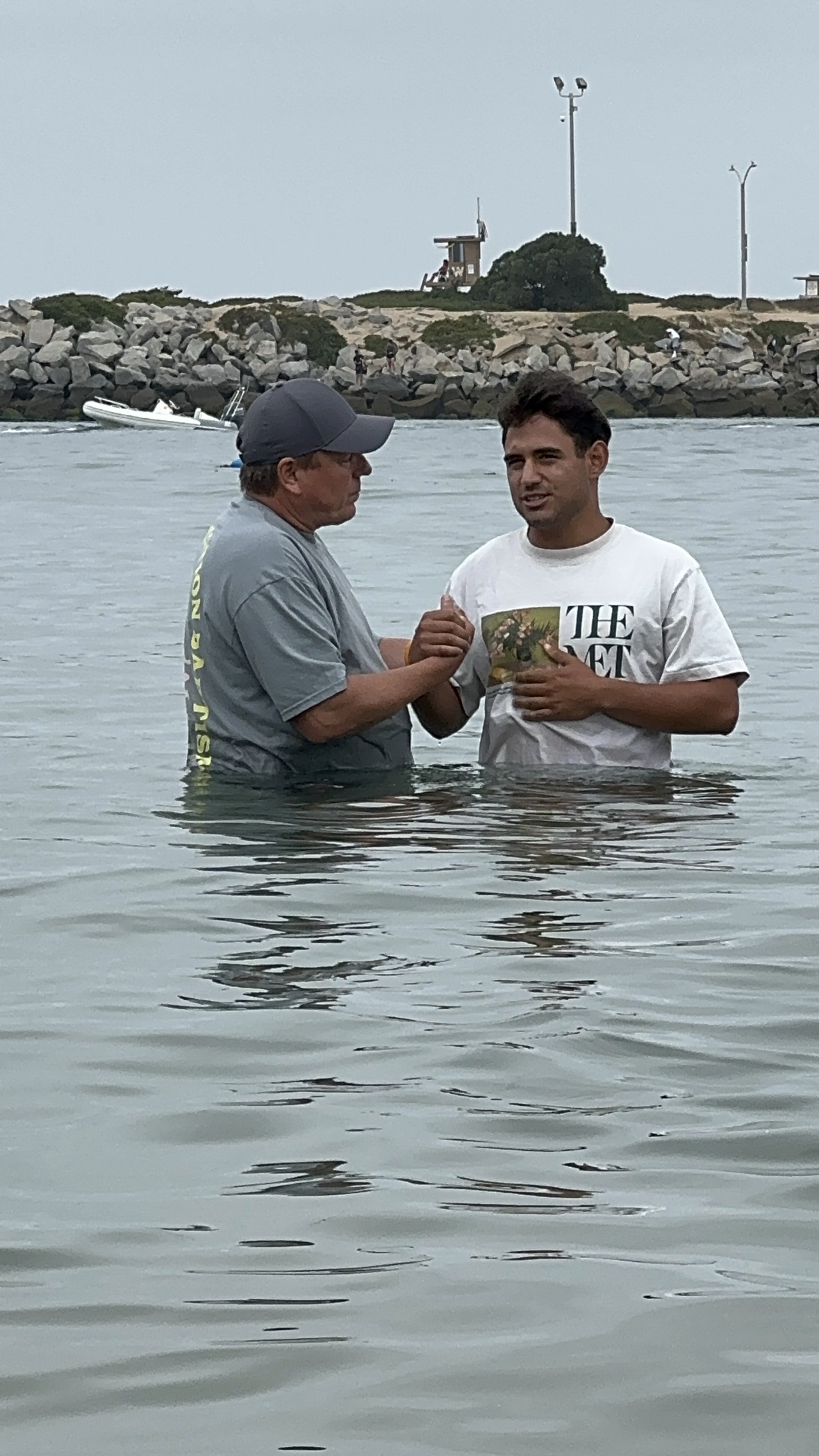 Matthew waist deep in the ocean being baptized, holding the pastor's hands